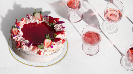 Summertime Cream whole cake sits on table with glasses of rosè wine with shadows cast